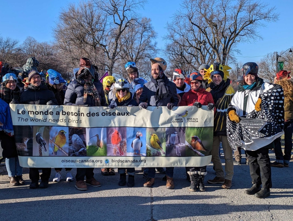 People dressed up as birds holding a sign with bird pictures on it